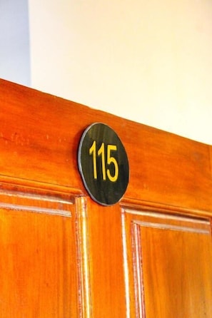 Une porte en bois sur laquelle est fixé un panneau circulaire noir portant le numéro 115.