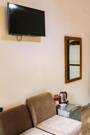 Ein Zimmer mit Flachbildfernseher an der Wand, einem spiegelnden Holzbettrahmen, einer Couch, einem kleinen Tisch mit Wasserkocher und einer Kaffeemaschine.