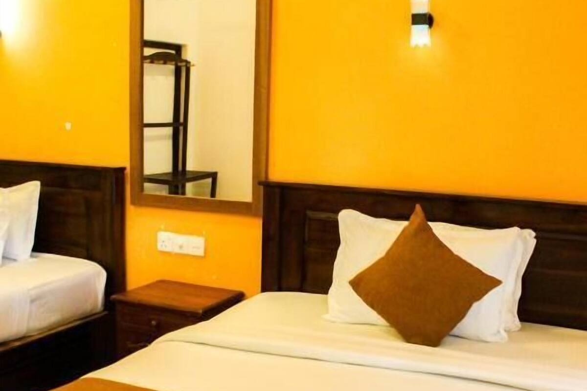 A hotel room with a bed, a nightstand, a mirror, and a wall-mounted light.