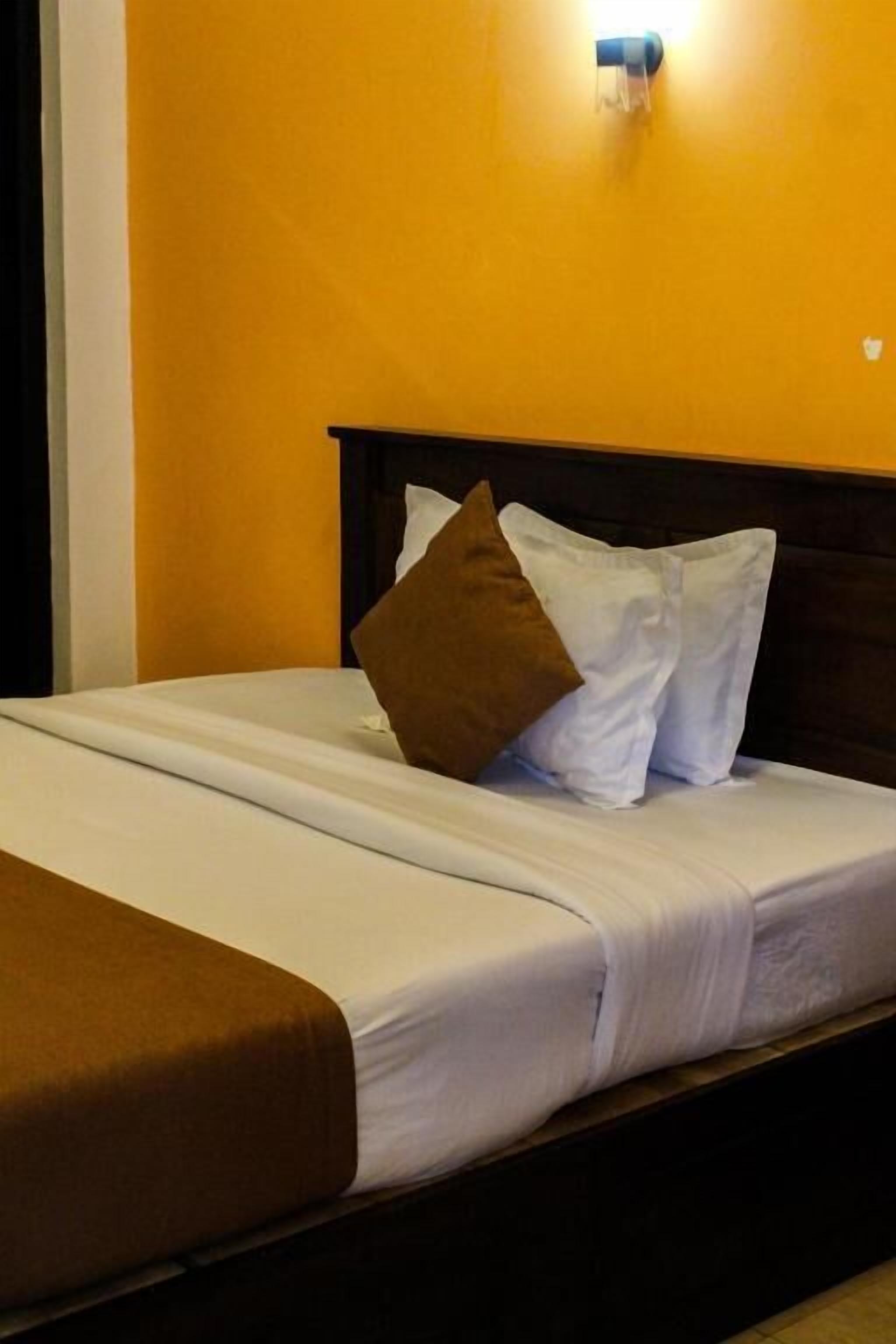 A bed with white linens, brown pillows, and a brown throw blanket.