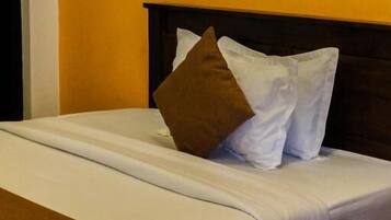 A bed with white linens, brown pillows, and a brown throw blanket.