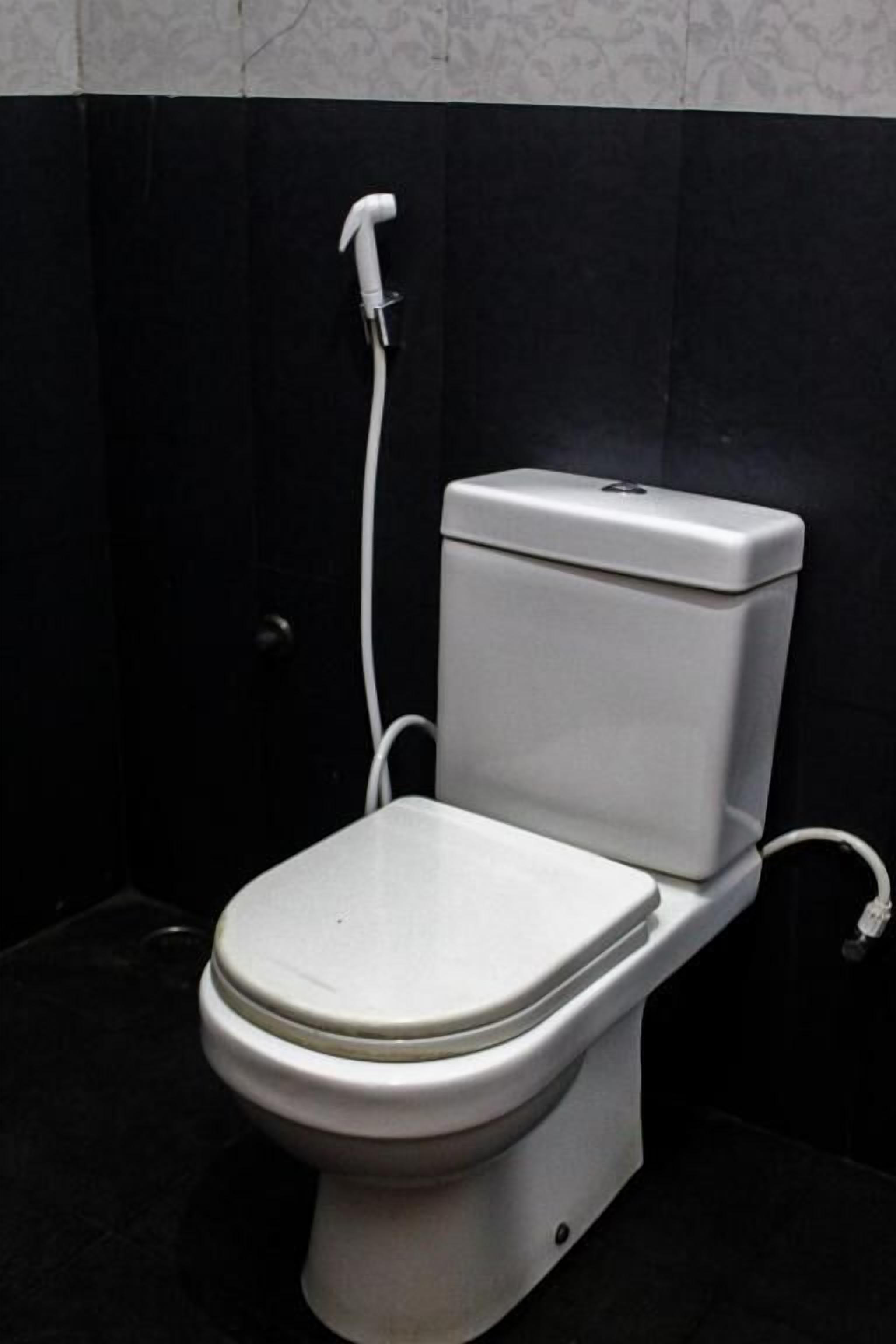 Inodoro con asiento y tanque blancos, un manguera blanca y una pared de azulejos negros.