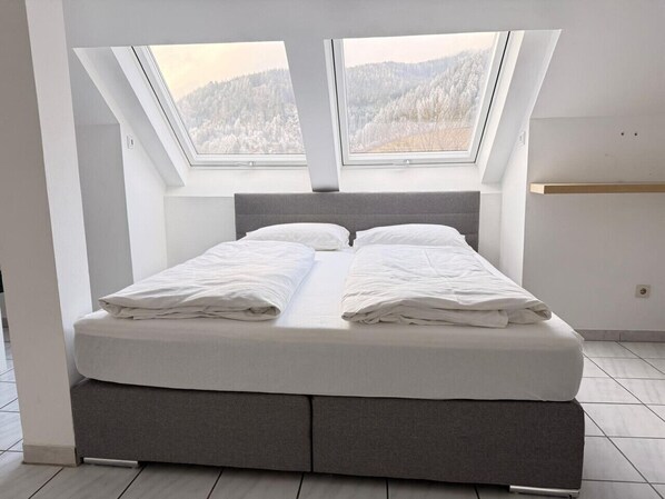 Un dormitorio moderno con tragaluz, una cama con ropa de cama blanca y vistas a un paisaje nevado.