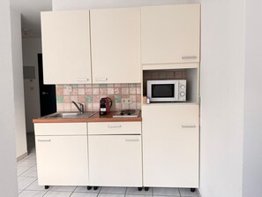 Una cocina compacta con microondas, hervidor y pileta.