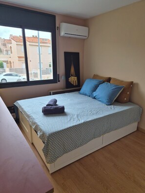 A bedroom with a bed, a window, an air conditioner, and a painting on the wall.