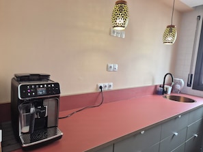 A kitchenette with a coffee machine, two pendant lights, a sink, and a window.