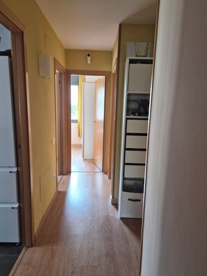 A hallway with wooden flooring, a white refrigerator, a white cabinet, and a door leading to another room.