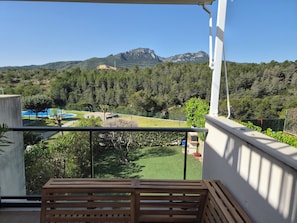 A balcony with a view of a mountainous landscape, a green lawn, and a blue structure in the distance.
