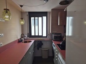 A compact kitchen with a washing machine, a microwave, and a window with blinds.