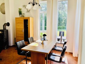 A dining area with a wooden table, black chairs, a chandelier, and a view of greenery outside. - Vrbo Property (Fuhlendorf)