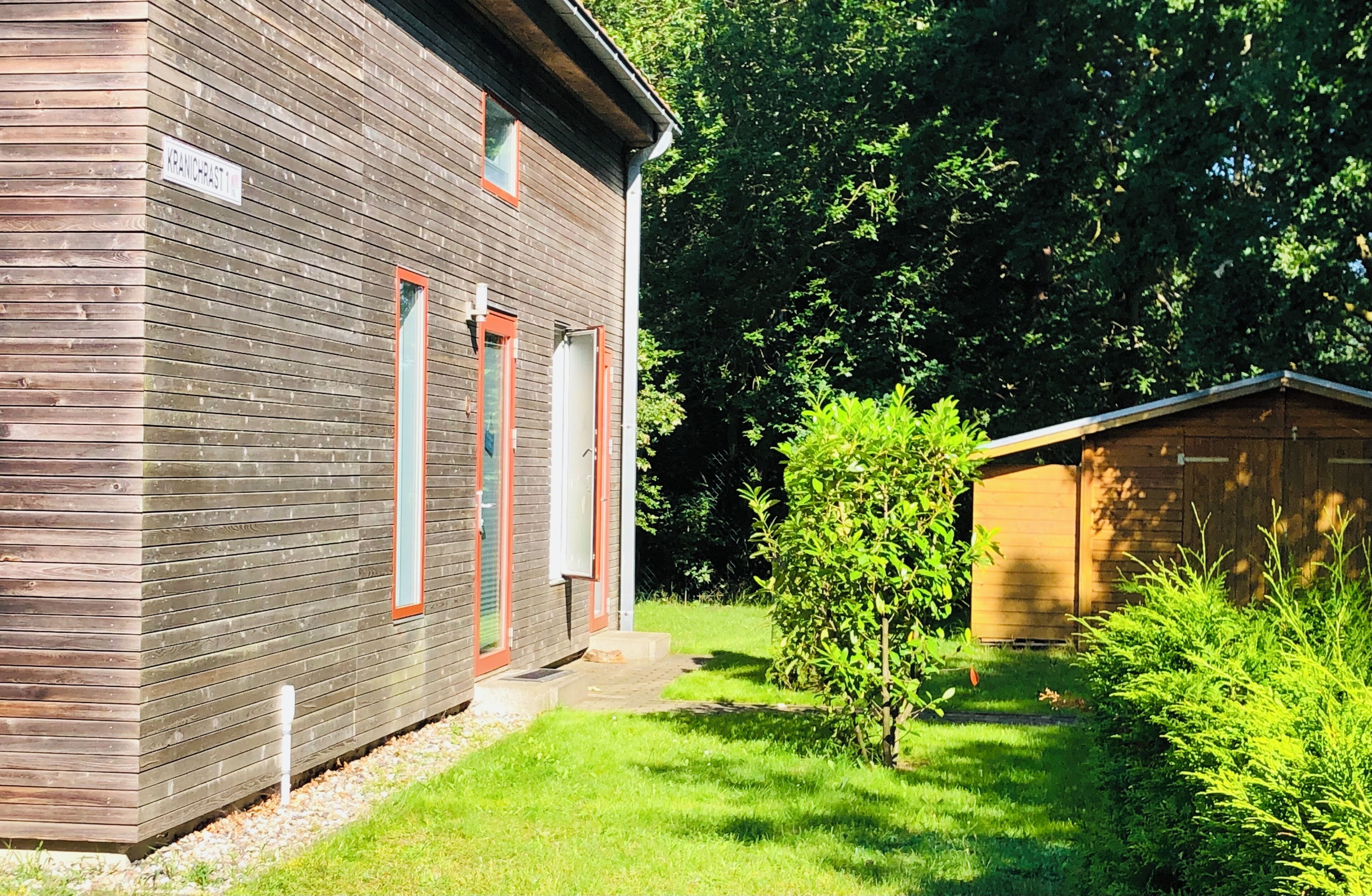 Een houten gebouw met een bord waarop 'VANDERAST1' staat, een klein raam en een deur.