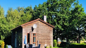 A wooden cabin with a satellite dish, a covered patio with a table and chairs, and a grassy yard. - Welcome to the vacation home "OstseeFreiheit", in the Fischland-Darß-Zingst region. (Fuhlendorf)