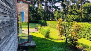 A wooden building with a glass door, a garden with grass, a bench, and trees in the background. - Welcome to the vacation home "OstseeFreiheit", in the Fischland-Darß-Zingst region. (Fuhlendorf)