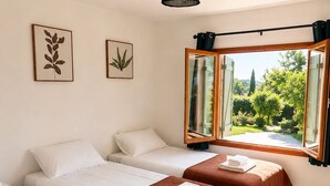 Een hotelkamer met drie bedden, een groot raam met uitzicht op groen en een plafondlamp.