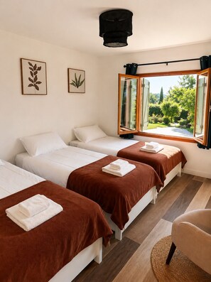 A hotel room with three beds, a large window with a view of greenery, and a ceiling light fixture. - At Domaine du Pape (Mazères)