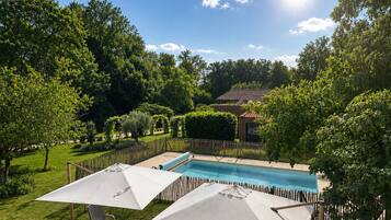 Un jardin à l’arrière de la maison, avec une piscine, entouré d’une végétation luxuriante et délimité par une clôture en bois.