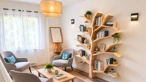 Een moderne woonkamer met een houten boekenkast, twee fauteuils, een salontafel en een lamp.
