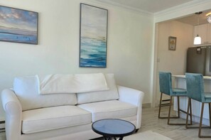 Ein Wohnzimmer mit einem weißen Sofa, einem runden Couchtisch und einem Meeresblick-Gemälde.