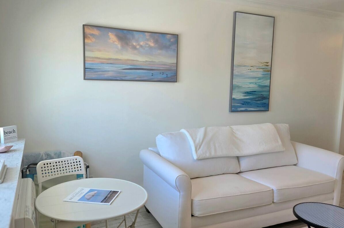 A white sofa, a round table, a white chair, and two paintings on the wall.
