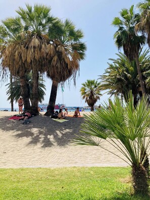 Een strand met palmbomen, mensen die zonnebaden, en een heldere lucht.