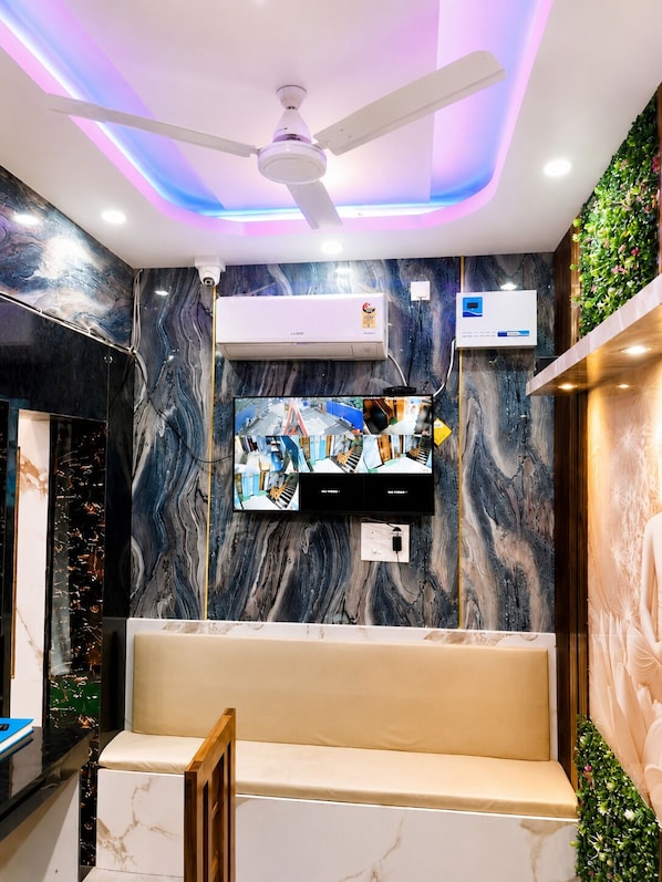 A modern interior with a ceiling fan, air conditioning unit, mounted TV, marble wall, and a bench. - Hotel Niladri Palace - near Sea Beach (Puri)