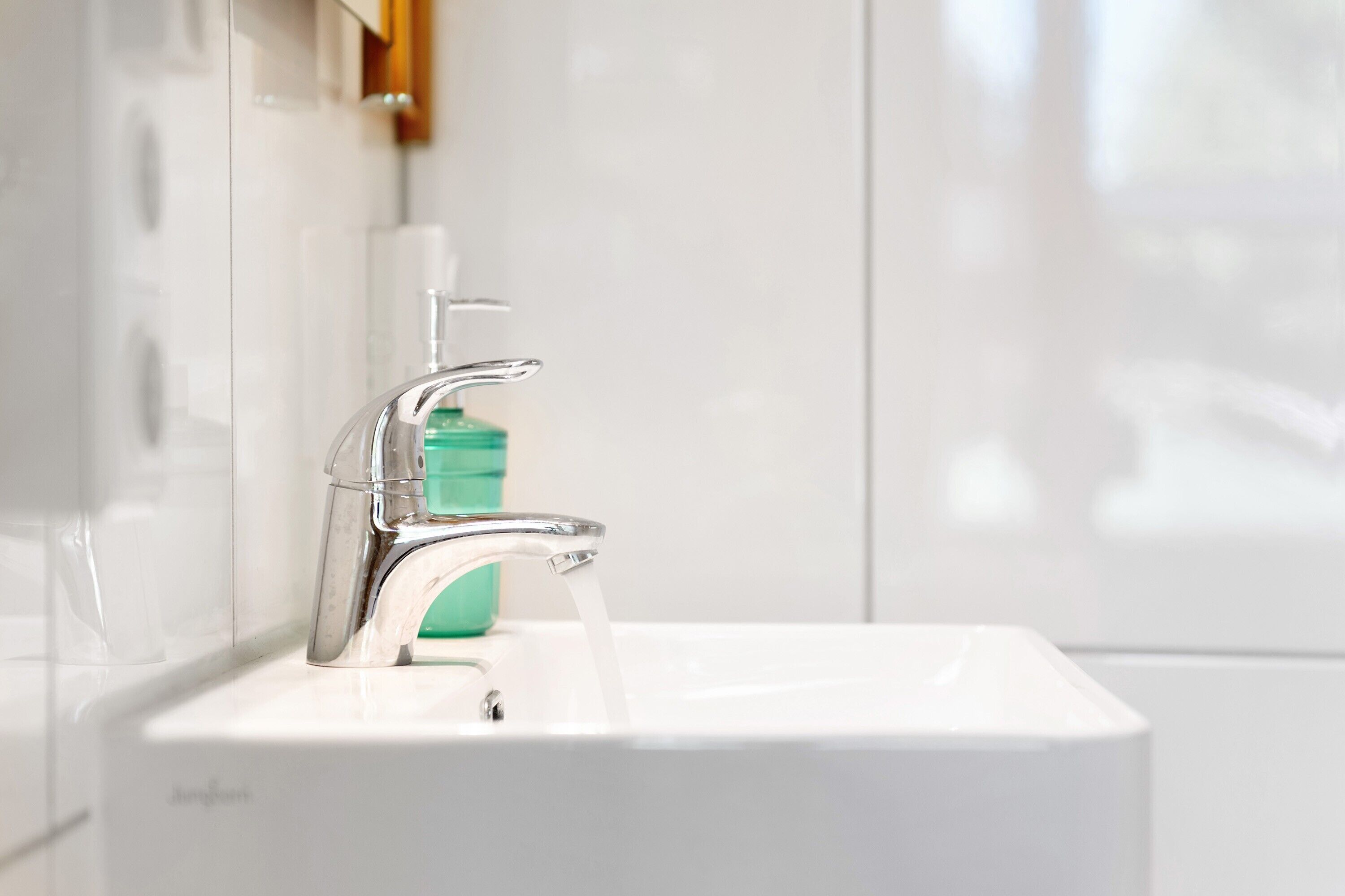 Ein modernes Badezimmer mit chromfarbenem Wasserhahn, einer transparenten Seifenspender und einem weißen Waschbecken.