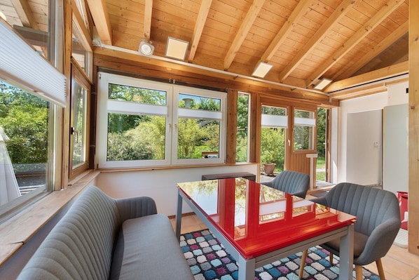 A modern interior with a wooden ceiling, large windows, a red table, and a gray sofa.