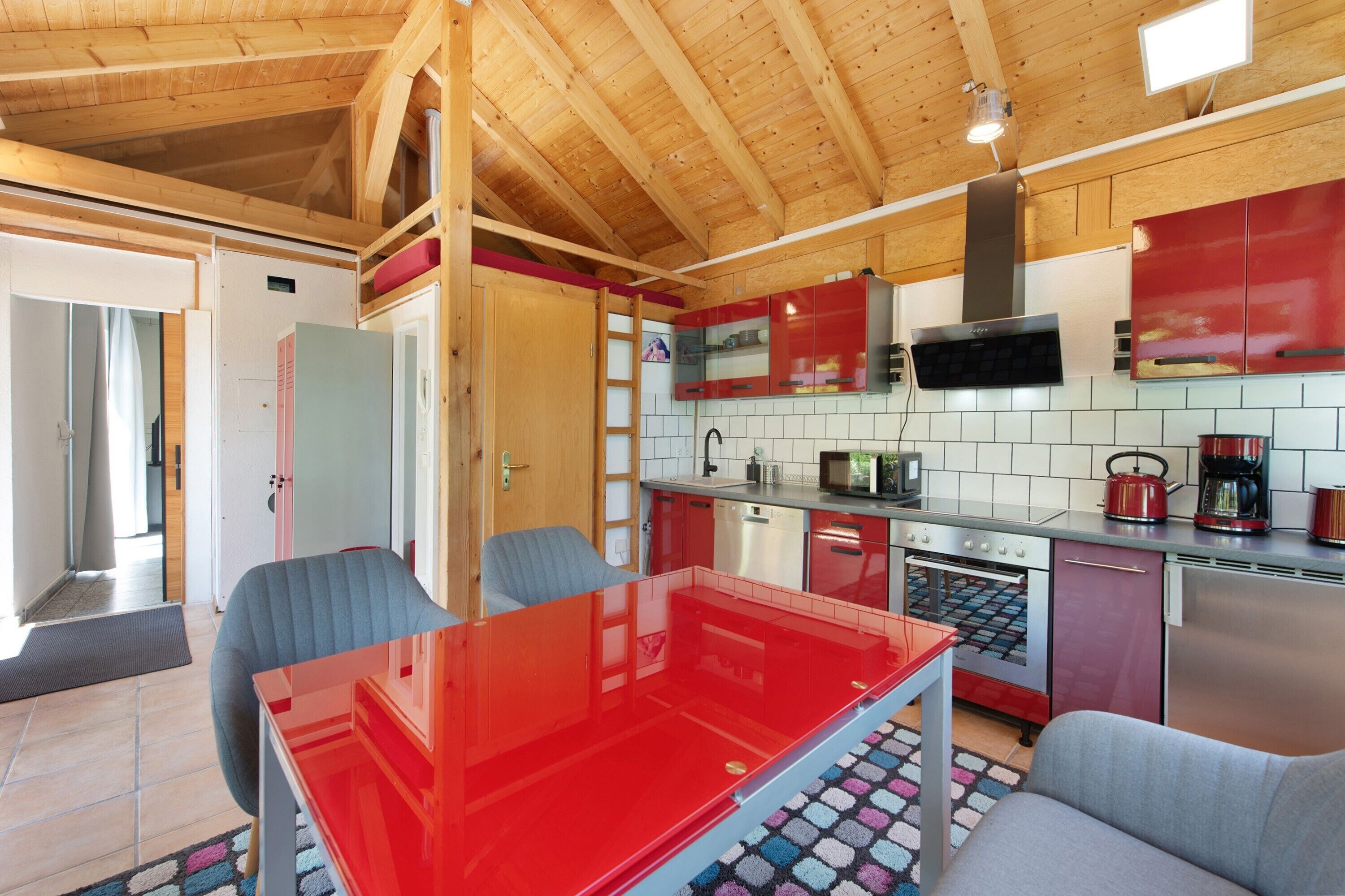 Eine moderne Küche mit Holzbalken, einem roten Tisch und einer gefliesten Spritzschutzwand.