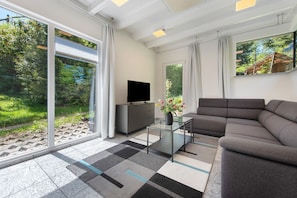 A modern living room with a sofa, a flat-screen TV, a glass coffee table, and large windows offering a view of greenery. - Holiday Home 'Ferienhaus Honberg' with Private Terrace, Private Garden and Wi-Fi (Tuttlingen)