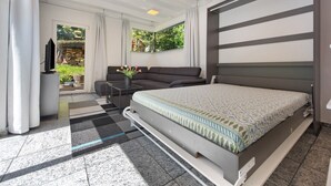 Ein modernes Schlafzimmer mit einem großen Bett, einer Sitzecke, einem Fernseher und einem Fenster mit Blick auf Grünflächen.