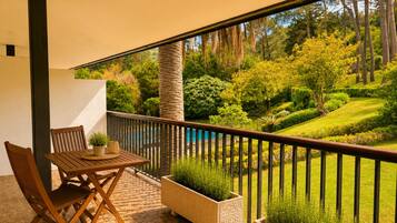 A balcony with a wooden table and chairs, potted plants, and a view of a landscaped garden.