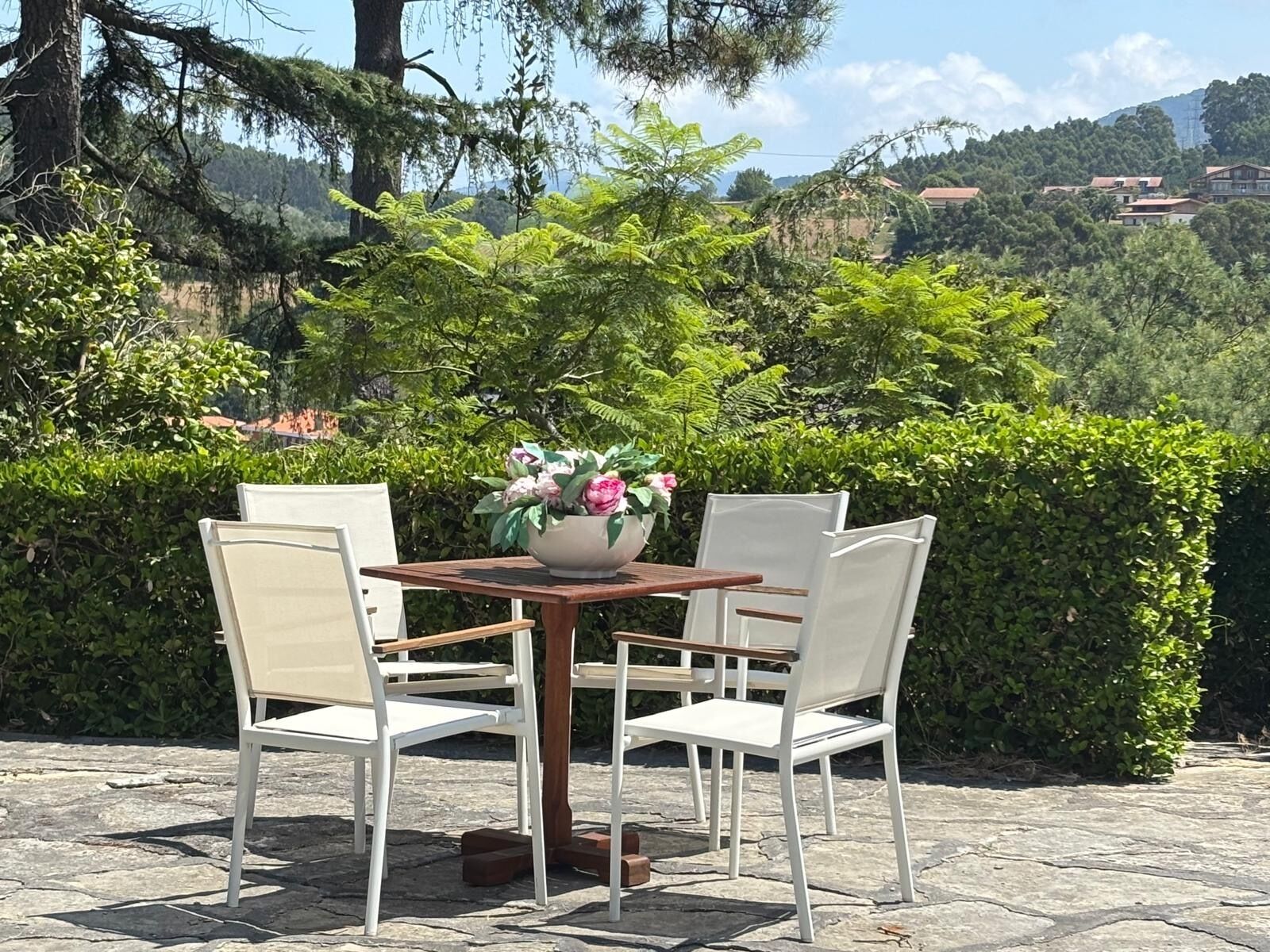 Una mesa exterior con sillas, un florero y un patio de piedra.