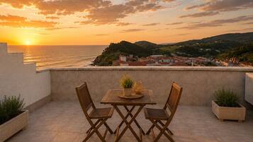 Una terraza con mesa y sillas, con vistas a un pueblo costero al atardecer.
