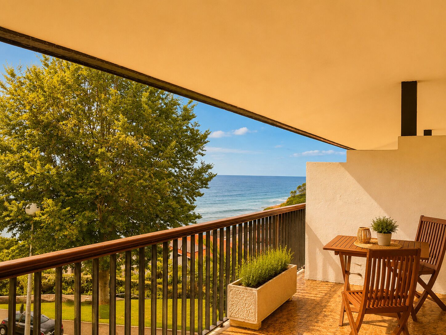 A balcony with a view of the ocean, a wooden table with chairs, and a potted plant.