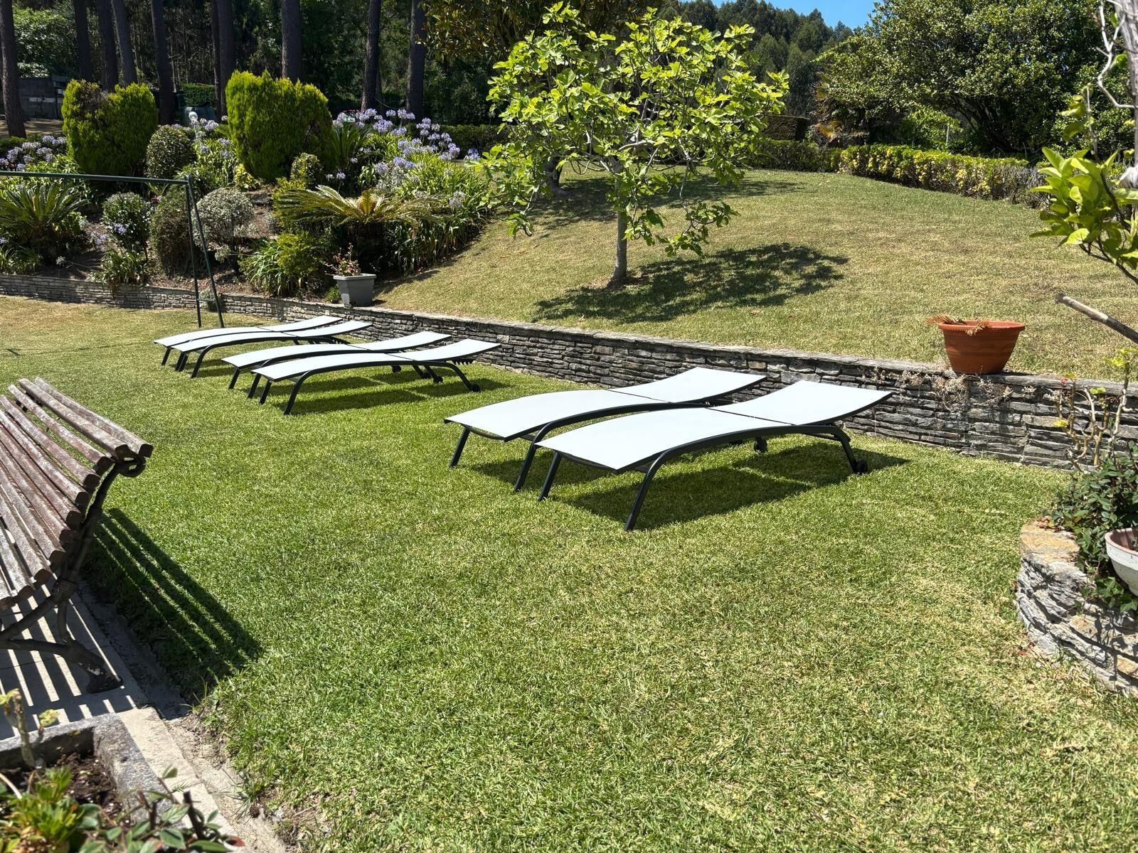 A garden with a row of lounge chairs and a stone wall.