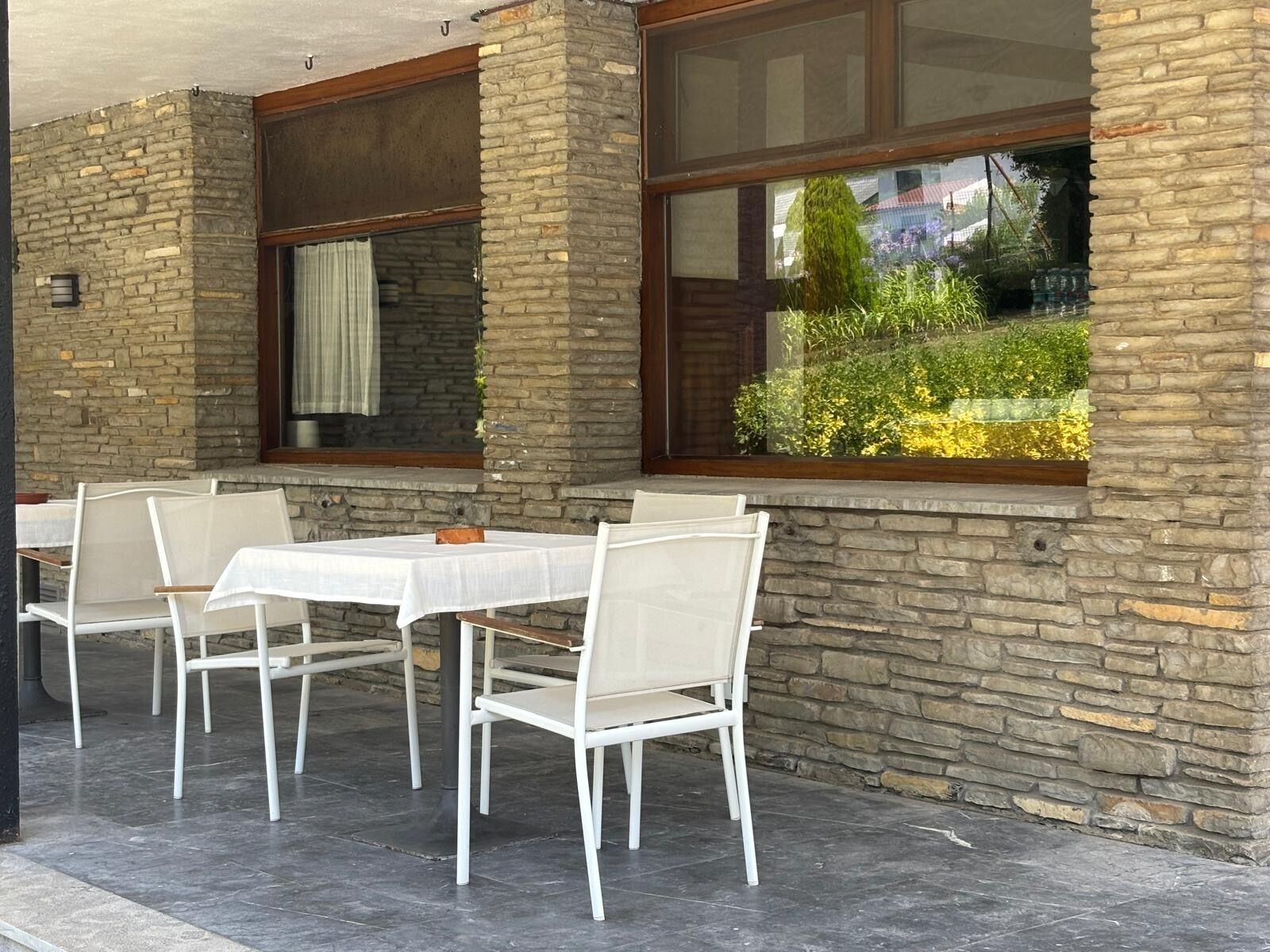 Un área de estar al aire libre con pared de piedra, ventana con vistas a vegetación y mesa con sillas.
