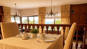 Une salle à manger avec une table dressée pour quatre personnes, une plante en pot et une vue dégagée sur l’extérieur grâce à de grandes fenêtres.