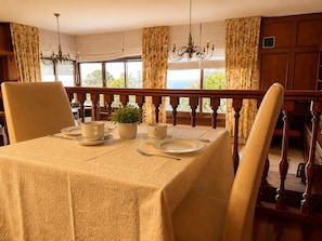 A dining room with a table set for four, a potted plant, and a view through large windows.