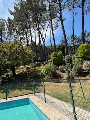 Piscina con valla de malla, rodeada de árboles y jardín ajardinado.