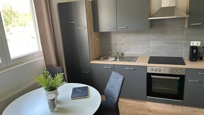 A compact kitchen with a dining area, a built-in oven, and a window with curtains. - FarawayHomes Studio Leoben #P72 (Donawitz)
