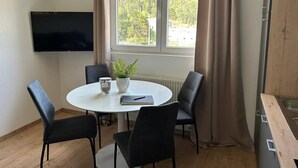 A room with a round table, four chairs, a potted plant, a flat-screen TV, and a window with curtains. - FarawayHomes Studio Leoben #P72 (Donawitz)