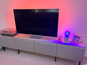 A flat-screen TV on a white entertainment unit with a vinyl record player, a small figurine, and a framed picture. - Studio lease mobility near Paris (Aulnay-sous-Bois)