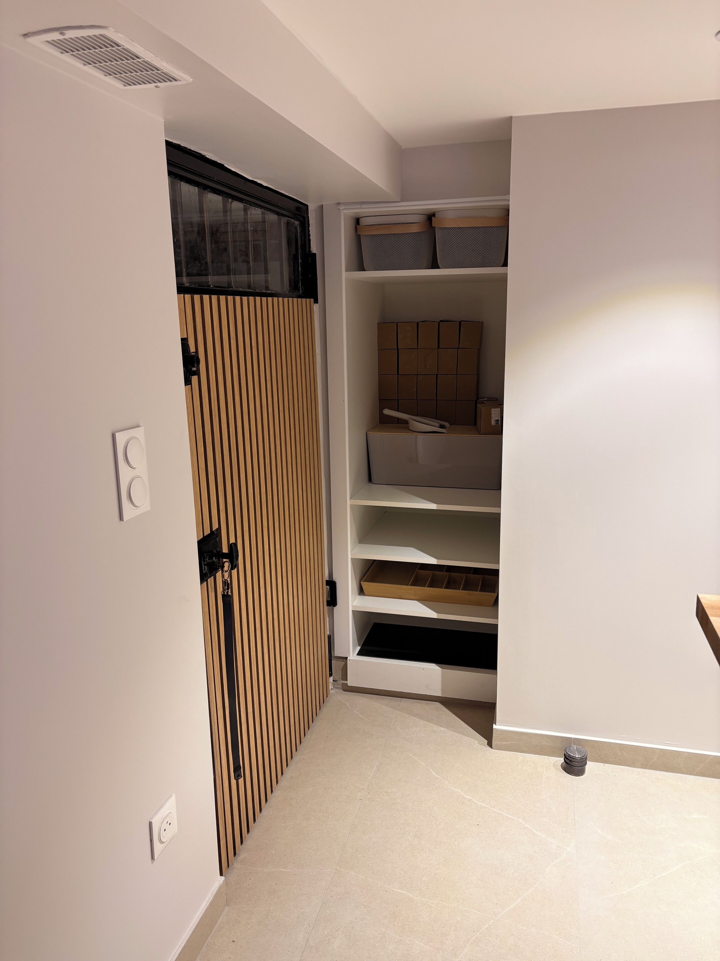 A narrow hallway with a sliding door leading to a closet with shelves and a bed.