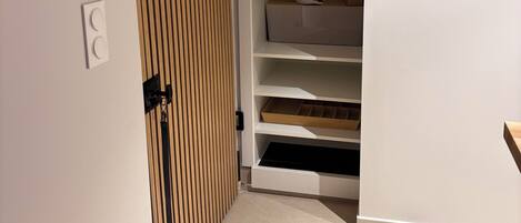 A narrow hallway with a sliding door leading to a closet with shelves and a bed.