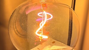 Een heldere glazen lamp met een zwart voetstuk en een gebogen handvat, bevestigd op een metalen standaard.