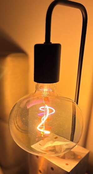 A clear glass light bulb with a black base and a curved handle, mounted on a metal stand. - Studio lease mobility near Paris (Aulnay-sous-Bois)