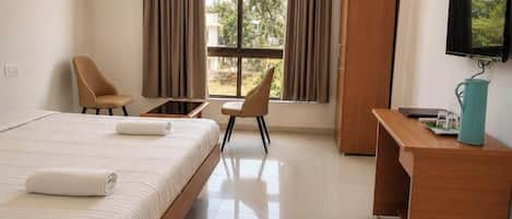 A hotel room with a bed, two chairs, a desk, a television, and a window with curtains.