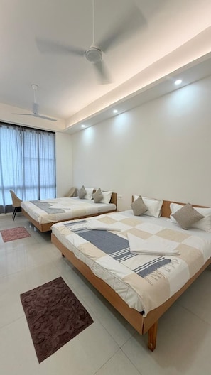 A modern bedroom with two beds, a ceiling fan, and a large window with curtains. - The Purple Mango  (Mawal)