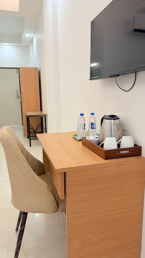 A hotel room with a wooden desk, a chair, a television mounted on the wall, and a coffee maker on the desk. - The Purple Mango  (Mawal)
