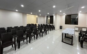A conference room with rows of chairs, a table with a tablecloth, and a ceiling fan. - The Purple Mango - Pure Veg (Lonavala)